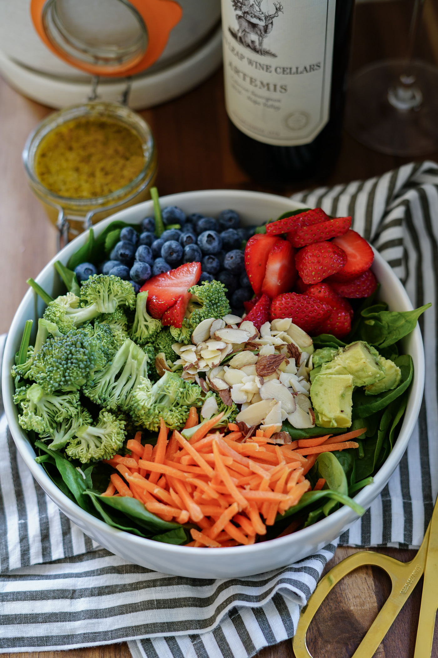 A large bowl with spinach, strawberries, blueberries, avocado, carrots and almond slides for an anti-inflammatory salad